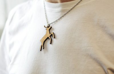 The wooden christmas necklace with shape of deer on the man's neck in a white t-shirt